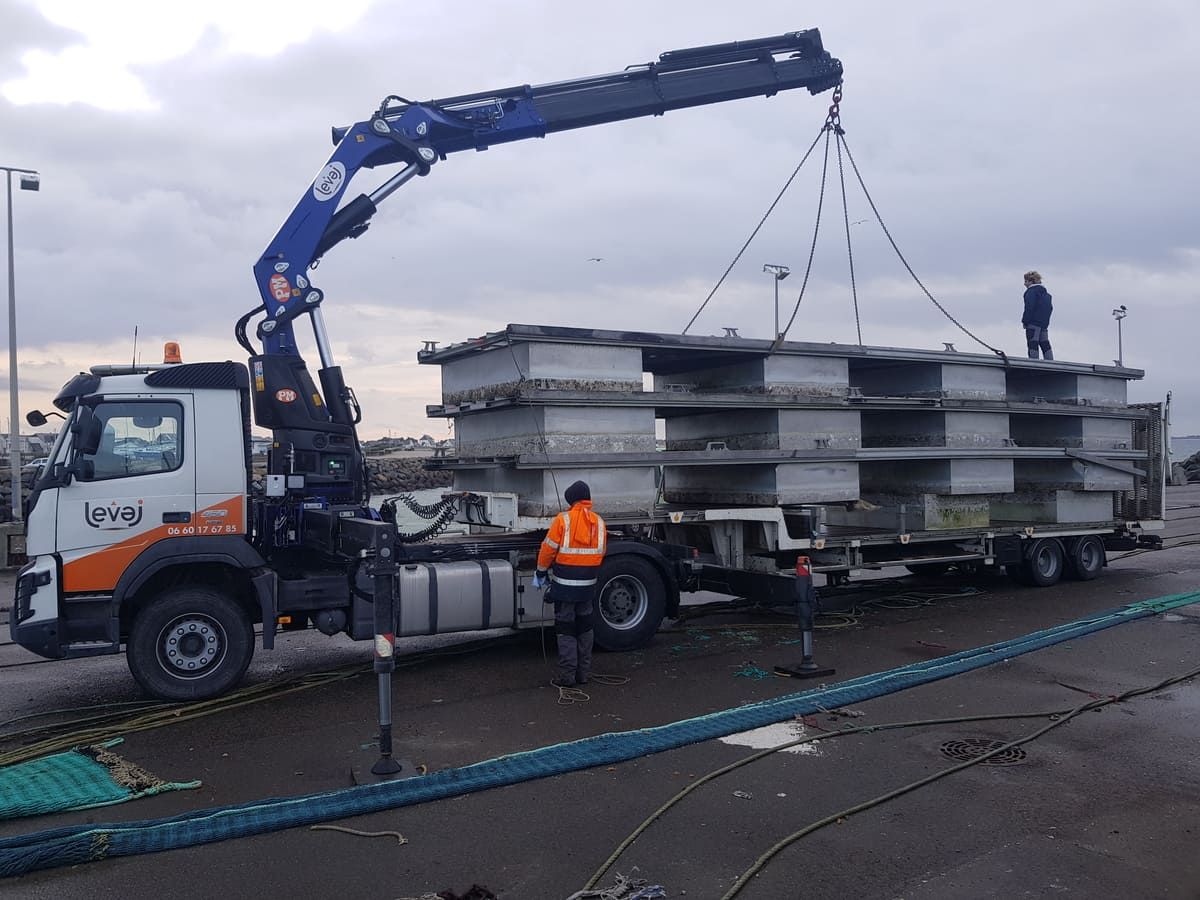 Grue bleue du Volvo FMX levant des structures métalliques sur la semi-remorque, sur un quai