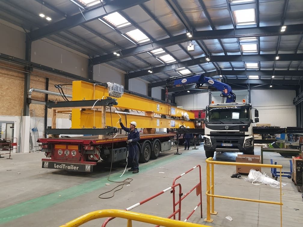 Chargement de poutres de pont roulant jaunes dans un hall industriel