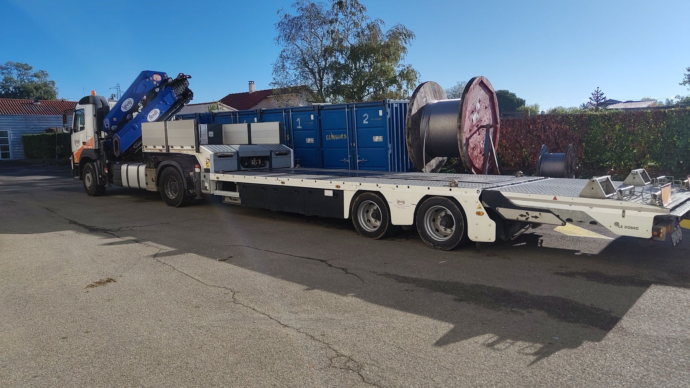 La semi-remorque surbaissée de LEVAJ attelée au Volvo FMX, plateau vide, devant des conteneurs